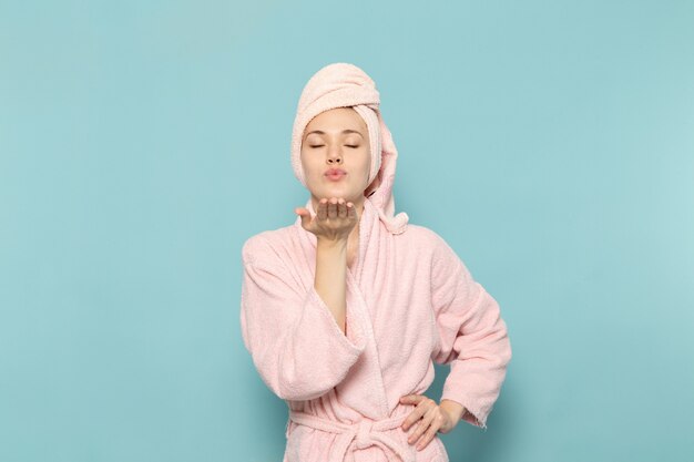 Mujer joven en bata de baño rosa después de la ducha enviando besos al aire en azul