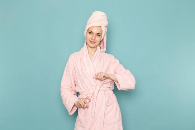 Mujer joven en bata de baño rosa después de la ducha posando con una sonrisa en azul