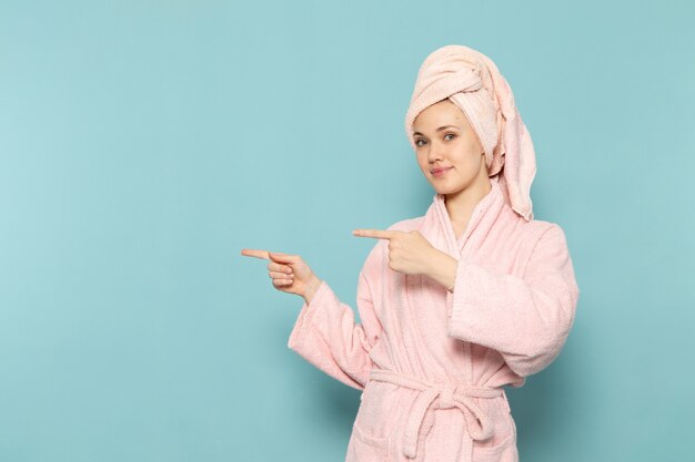 Mujer joven en bata de baño rosa después de la ducha posando con una sonrisa en azul