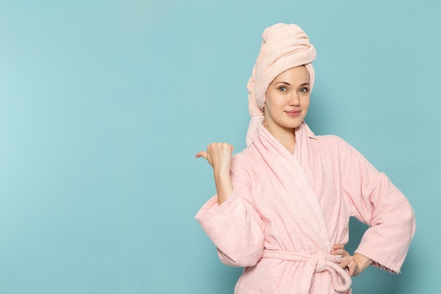 Mujer joven en bata de baño rosa después de la ducha simplemente posando en azul