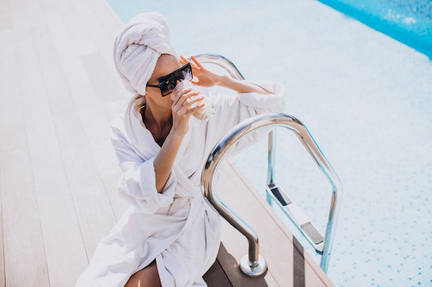 Mujer joven en bata de baño tomando café en la piscina