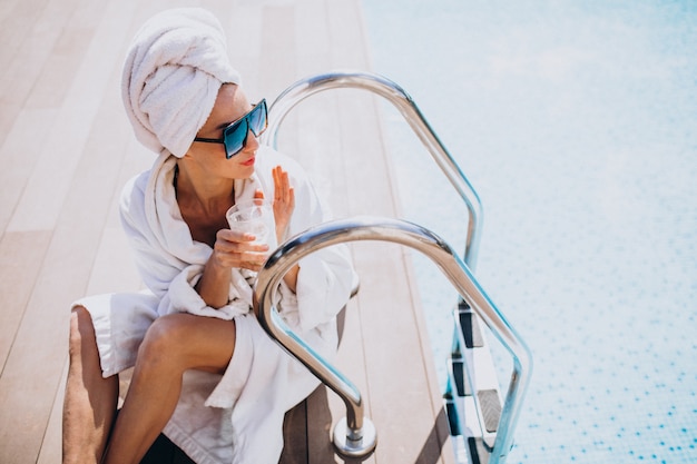 Mujer joven en bata de baño tomando café en la piscina