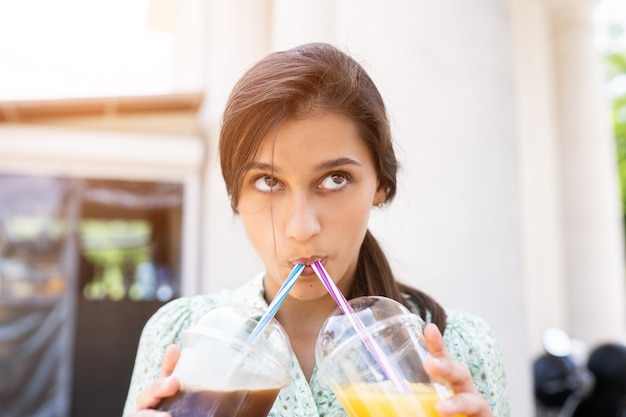 Mujer joven bebe dos cócteles con hielo en vasos de plástico con paja