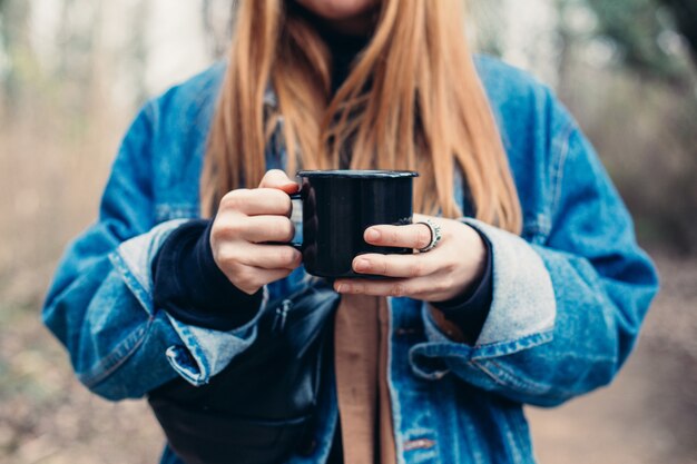 Mujer joven bebe taza de café en la orilla del lago