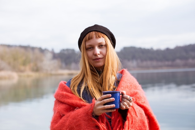 Mujer joven bebe taza de café en la orilla del lago