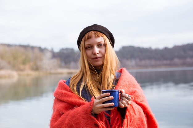 Mujer joven bebe taza de café en la orilla del lago