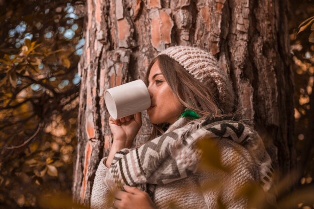 Mujer joven, bebida, cerca, árbol