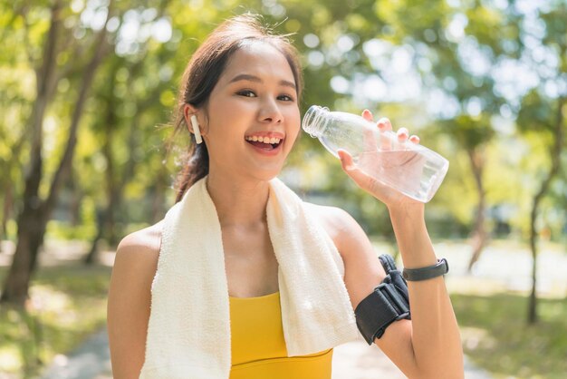 Mujer joven bebiendo agua de una botella mujer asiática bebiendo agua después de hacer ejercicio o deporte Hermosa atleta de fitness mujer con sombrero bebiendo agua después de hacer ejercicio al atardecer