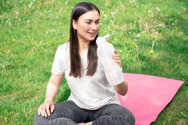 Una mujer joven bebiendo agua después de hacer ejercicio al aire libre