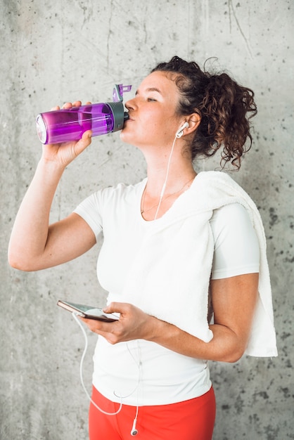 Foto gratuita mujer joven bebiendo agua y escuchando música en un teléfono inteligente