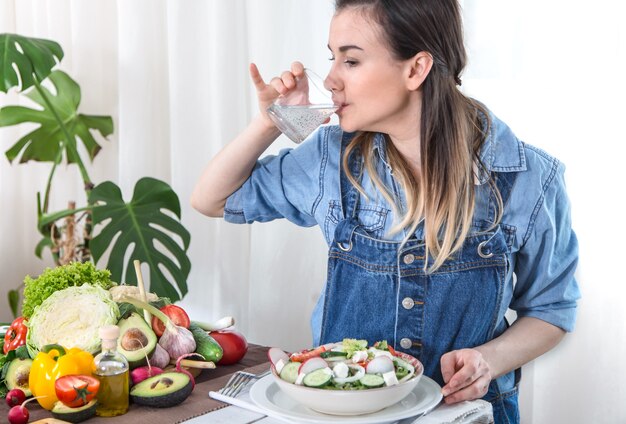 Mujer joven bebiendo agua en la mesa con verduras