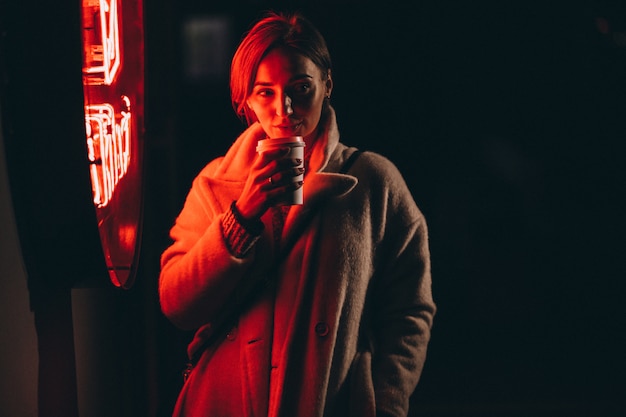 Mujer joven bebiendo café en la calle de noche