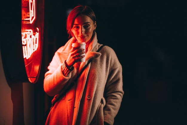 Mujer joven bebiendo café en la calle de noche