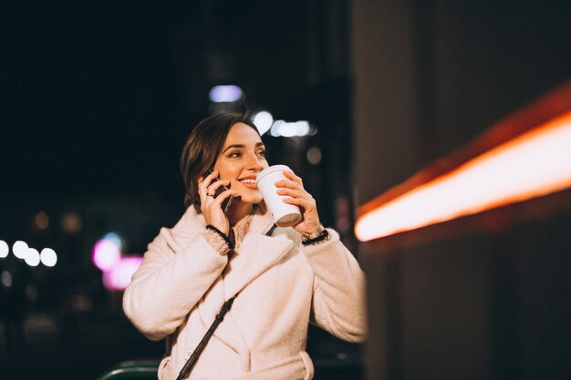 Mujer joven bebiendo café en la calle de noche