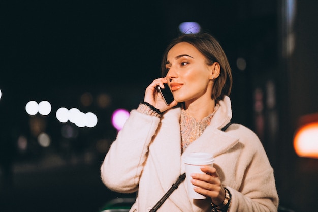 Mujer joven bebiendo café en la calle de noche