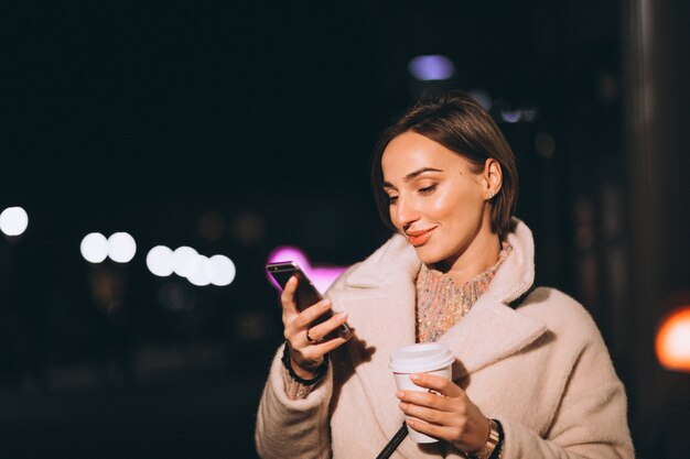 Mujer joven bebiendo café en la calle de noche