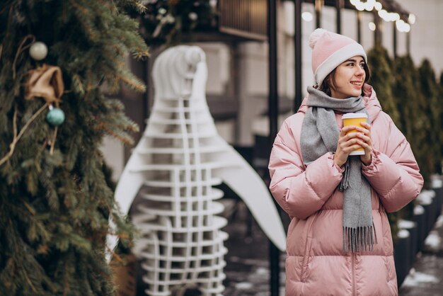 Mujer joven bebiendo café fuera de la calle de invierno