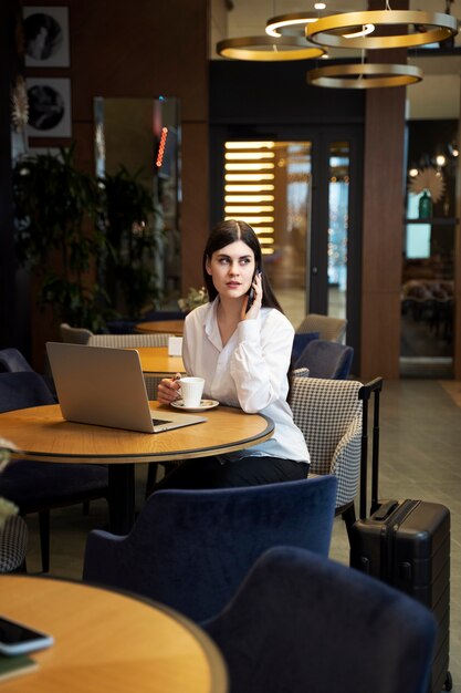 Mujer joven bebiendo café y hablando por su teléfono inteligente en un restaurante