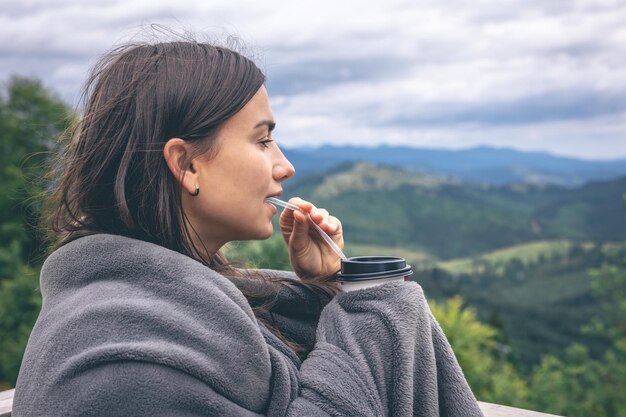 Una mujer joven bebiendo café con vistas a las montañas.