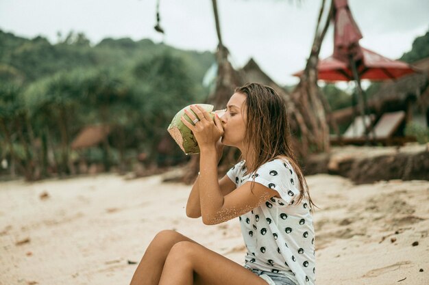 mujer joven bebiendo coco tropical en la playa