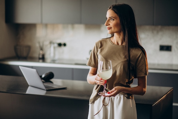 Mujer joven bebiendo limonada de vidrio en la cocina