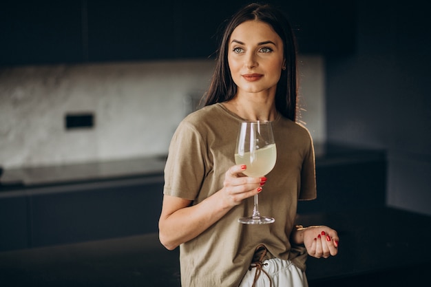 Mujer joven bebiendo limonada de vidrio en la cocina