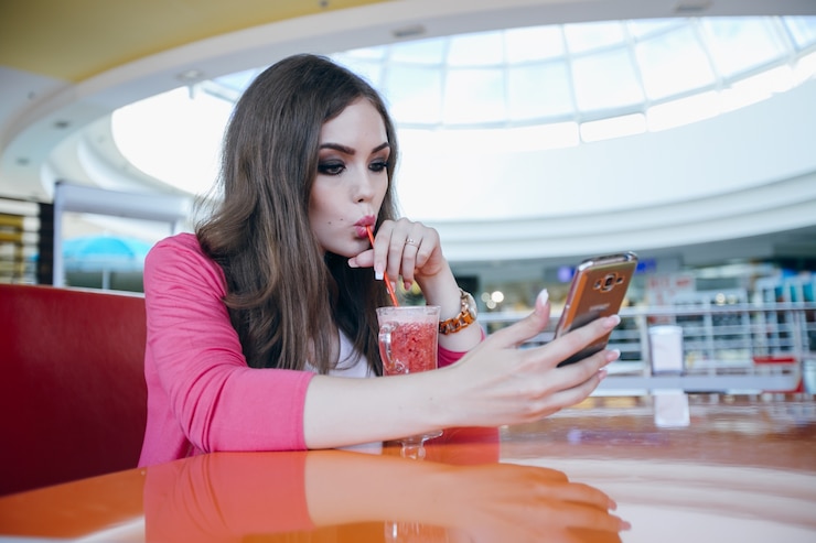 Foto gratuito mujer joven bebiendo un refresco mientras usa su móvil