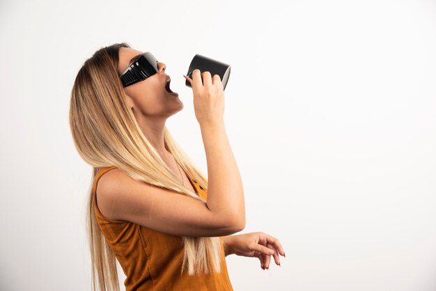 Mujer joven bebiendo de taza negra y gafas protectoras.