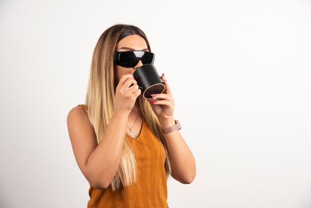 Mujer joven bebiendo de taza negra y gafas protectoras.