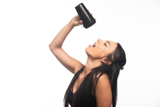 Mujer joven bebiendo de una taza en la pared blanca