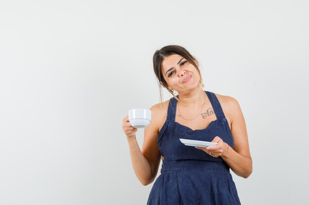 Mujer joven bebiendo té aromático en vestido y mirando encantado