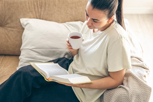 Mujer joven bebiendo té caliente leyendo su libro de papel favorito en casa