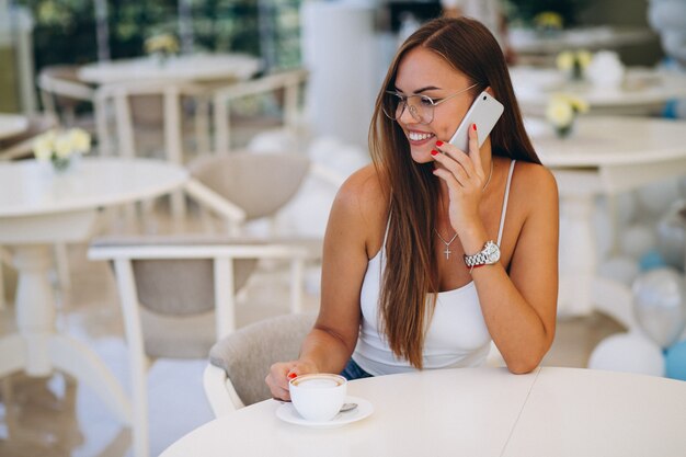 Mujer joven bebiendo té y usando el teléfono