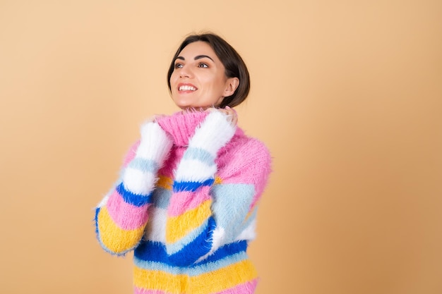 Mujer joven en beige en un suéter de punto acogedor multicolor brillante lindo sonriendo