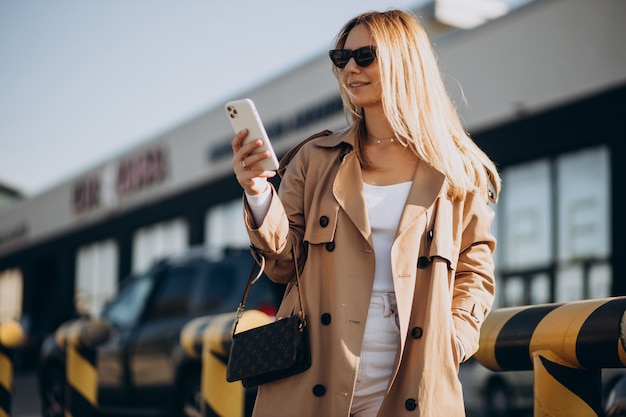 Mujer joven, en, beige, trinchera, utilizar, teléfono, exterior