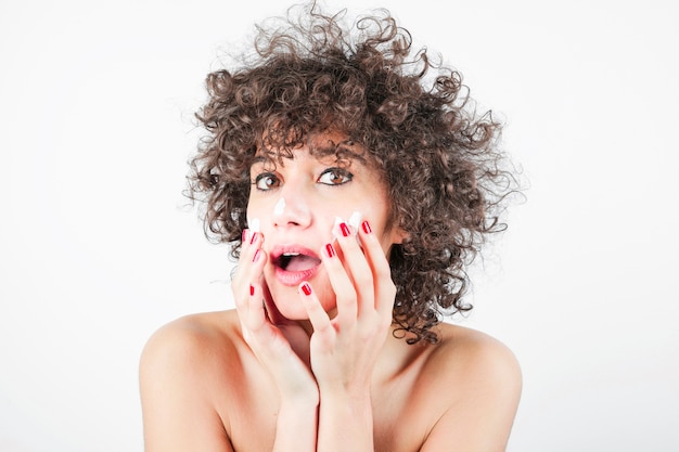 Foto gratuita mujer joven de la belleza con una boca abierta que aplica la crema en su cara