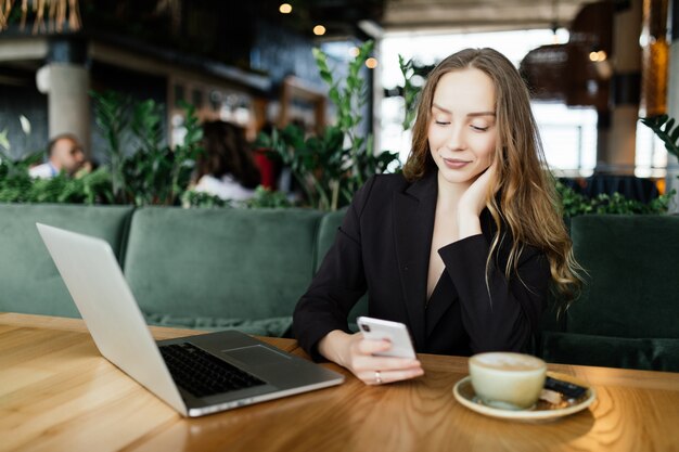 Mujer joven belleza en la cafetería hablar por teléfono con ordenador portátil y tomar café.