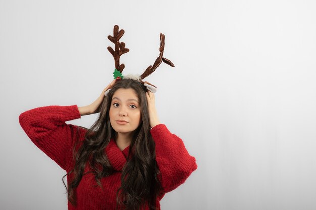 Mujer joven belleza con diadema de Navidad como cuernos de ciervo en suéter rojo de invierno.