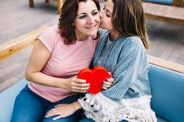 Mujer joven besando a mujer con regalo de San Valentín