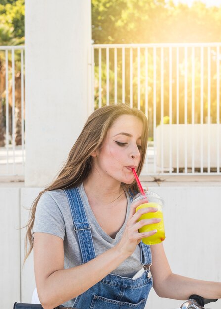 Mujer joven con bicicleta bebiendo jugo