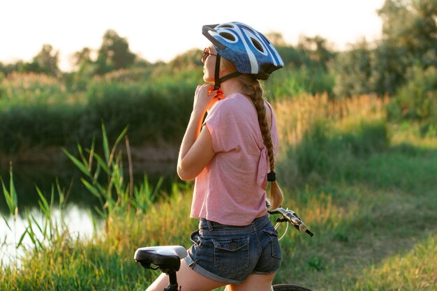 Mujer joven en bicicleta en el paseo junto al río y el prado inspirado en la naturaleza rodeada