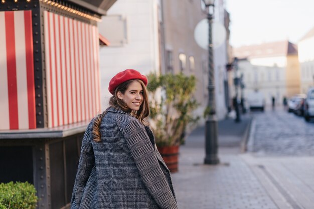 Mujer joven bien vestida mirando hacia atrás mientras camina por la calle temprano en la mañana