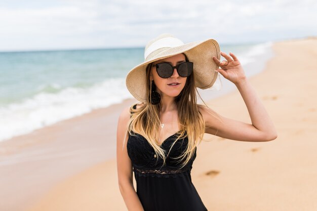 Mujer joven en bikini y sombrero para el sol relajante en la playa soleada.