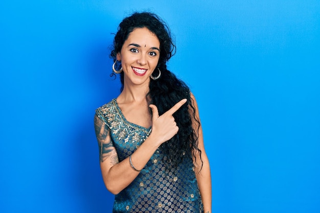 Foto gratuita mujer joven con bindi y vestido kurta tradicional alegre con una sonrisa de cara apuntando con la mano y el dedo hacia el lado con expresión feliz y natural en la cara