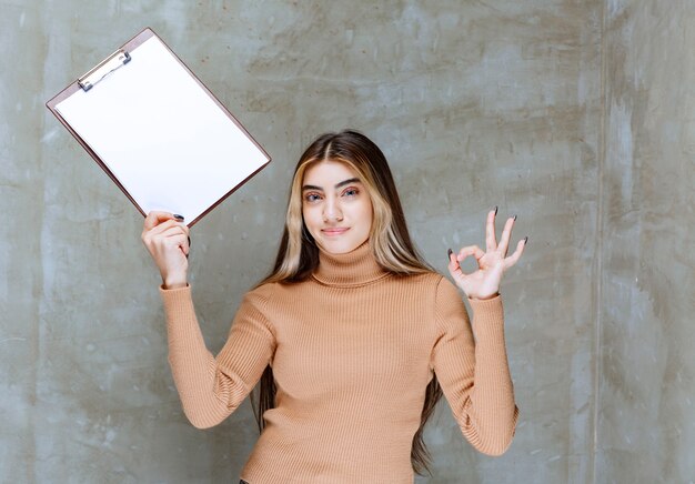 Mujer joven con bloc de notas mostrando gesto ok en una piedra