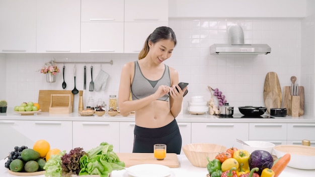 Mujer joven blogger asiática con smartphone para hablar, chatear y consultar las redes sociales en la cocina