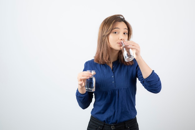 Mujer joven en blusa azul bebiendo un vaso de agua.