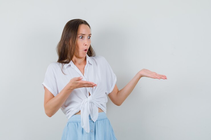 Foto gratuito mujer joven en blusa blanca y falda azul claro estirando las manos como presentando algo y mirando sorprendido