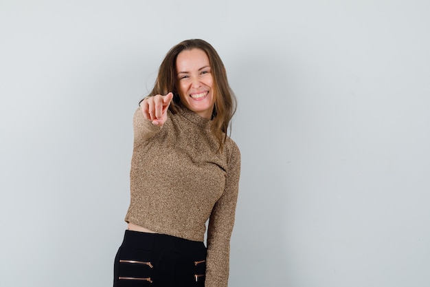 Foto gratuita mujer joven en blusa dorada apuntando al frente y mirando alegre