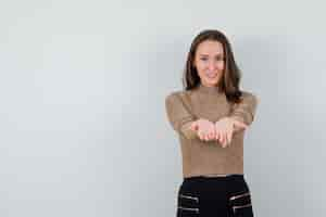 Foto gratuita mujer joven en blusa dorada posando como sosteniendo algo en las manos y mirando complacido, vista frontal. espacio para texto